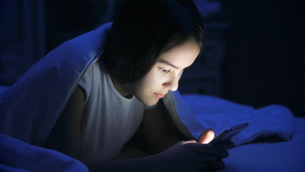 girl lying in bed at night and using smart phone